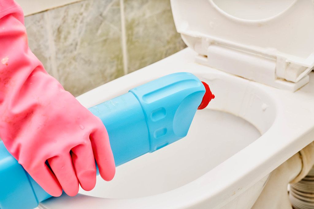 Woman is cleaning toilet bowl using detergent