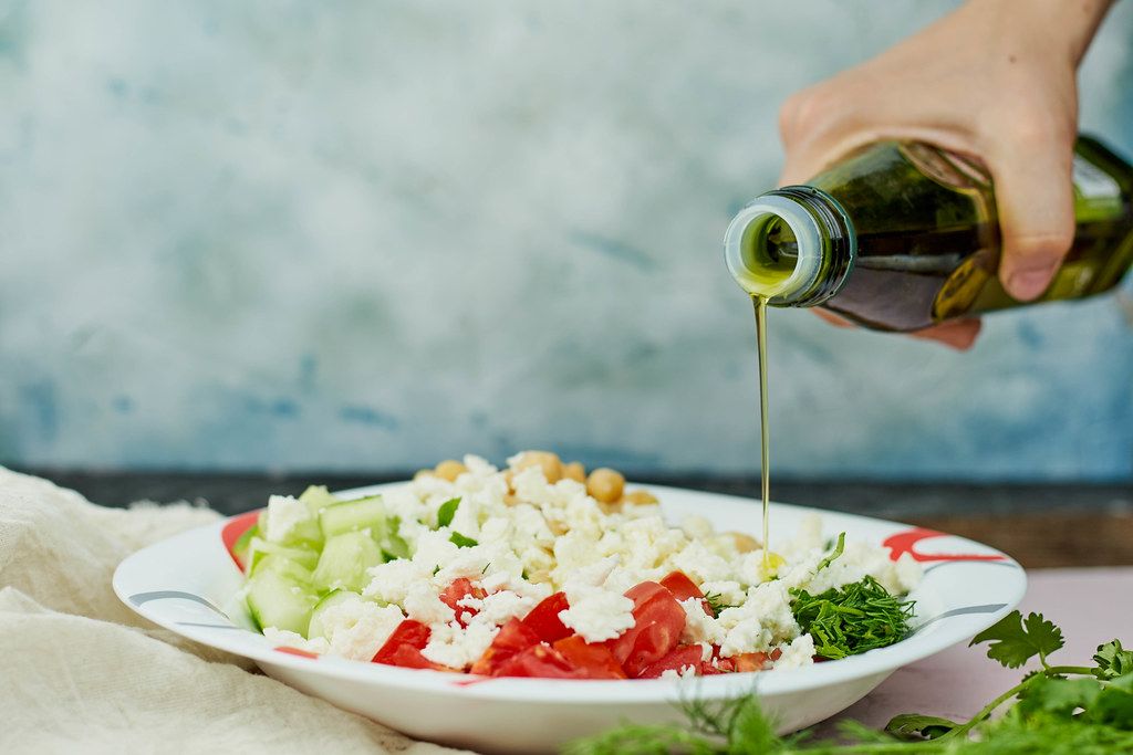 Woman pouring olive oil on a healthy salad