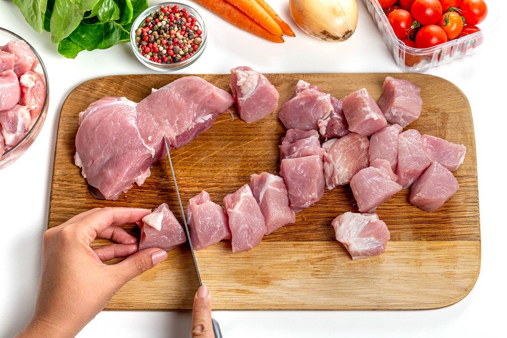 Woman slices pork meat on the kitchen board. Cooking concept