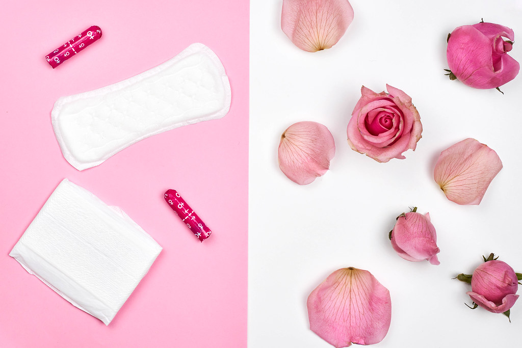Women's products: sanitary pad, panty liner, tampons on pink background with roses and petals decoration