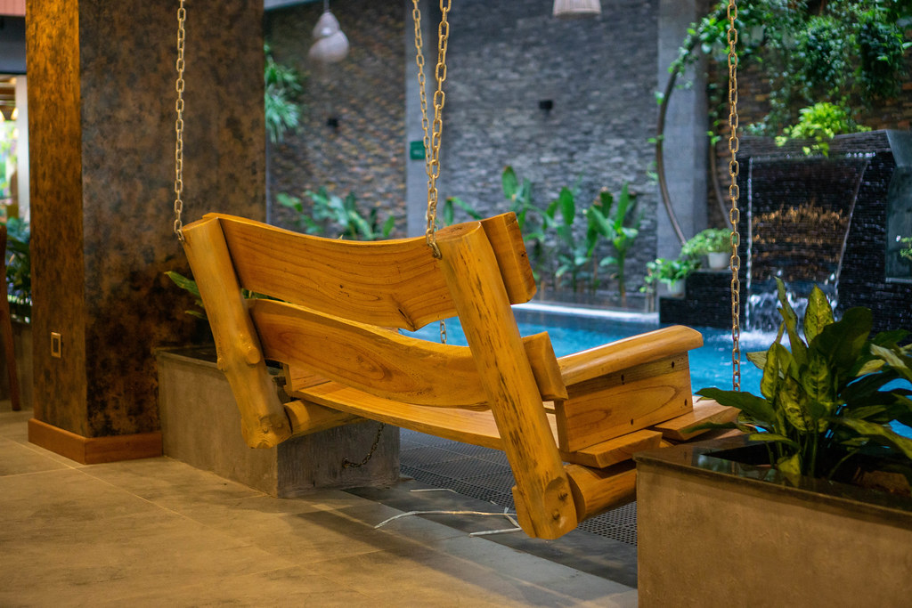 Wooden Bench Swing next to a Swimming Pool inside Chi House Hotel with many Plants and a Small Waterfall in Da Nang, Vietnam
