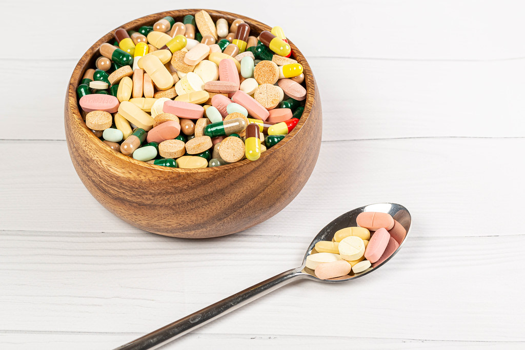 Wooden bowl with a spoon filled with medicine pills on a white wooden table