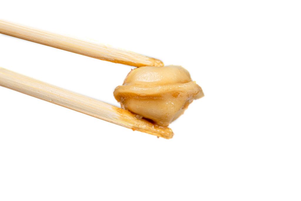 Wooden chopsticks holding a dumpling on a white background