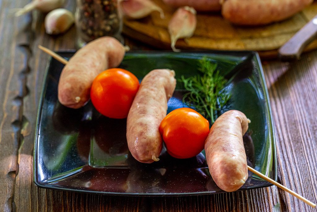Wooden skewer with raw sausages and tomatoes on a black plate