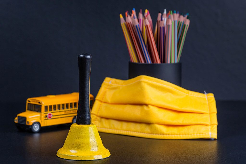 Yellow bell, mask, school bus and pencils as a symbol of the beginning of the new school year