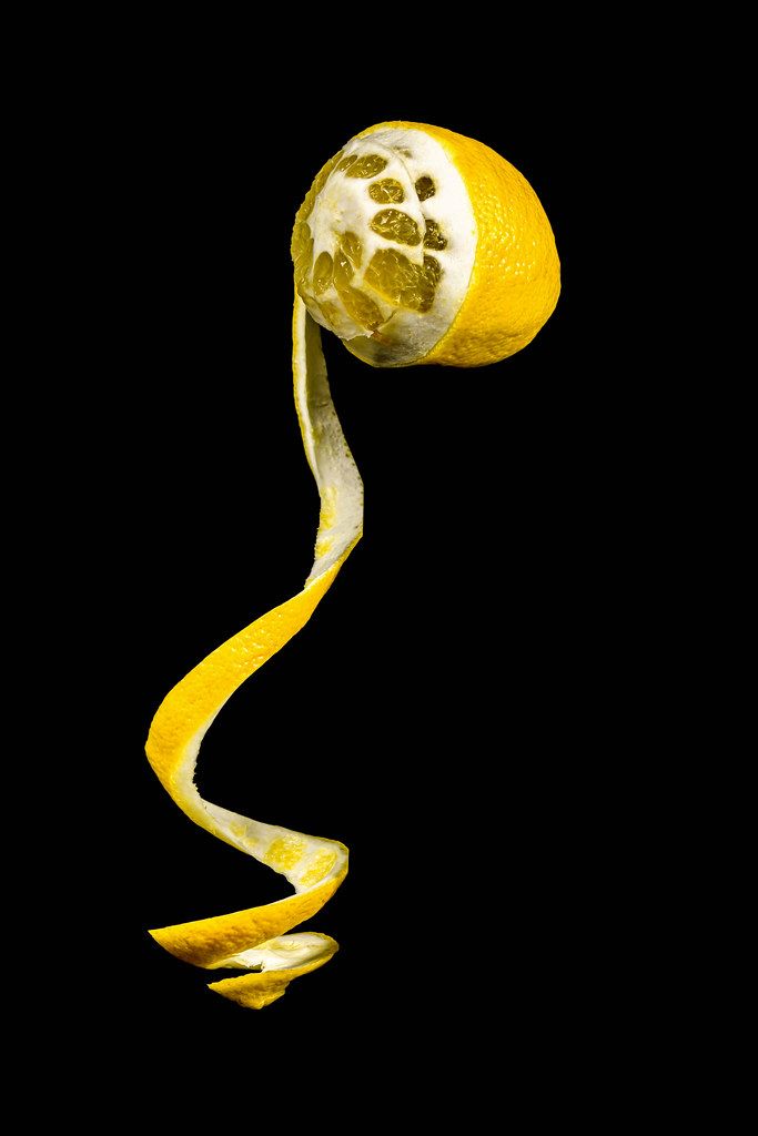 Yellow lemon with half peeled peel on dark background