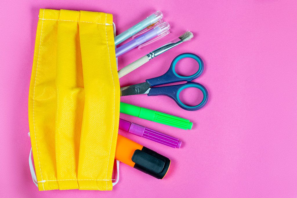 Yellow medical mask with school supplies on pink background