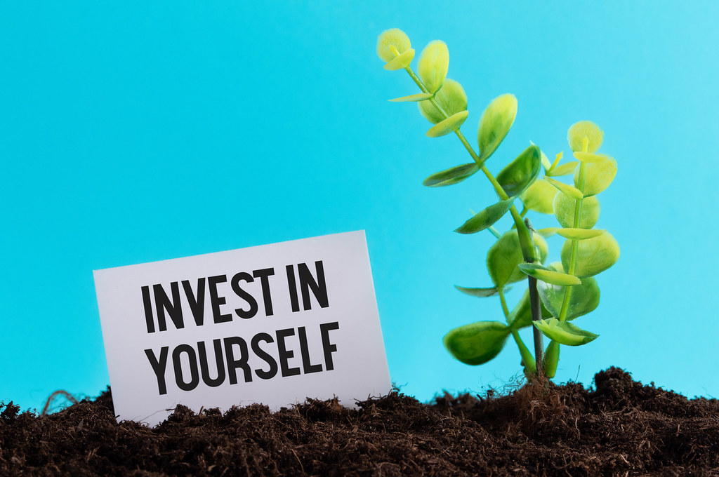 Young plant and piece of paper with Invest in Yourself text