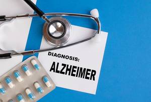 "Diagnose: Alzheimer", geschrieben auf blauem Ärzteordner, neben Medikamenten und Stethoskop
