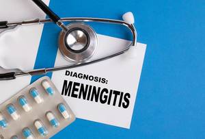 "Diagnose Meningitis / Hirnhautentzündung", geschrieben auf blauem Ärzteordner, neben Medikamenten und Stethoskop