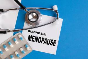 "Diagnose: Wechseljahre / Menopause", geschrieben auf blauem Ärzteordner, neben Medikamenten und Stethoskop