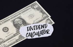 "Dividend calculator" Text auf kariertem Zettel mit zwei 100-Dollar-Scheinen vor schwarzem Hintergrund