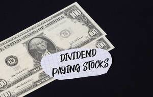 "Dividend paying stocks" Text auf kariertem Zettel mit zwei 100-Dollar-Scheinen vor schwarzem Hintergrund