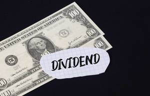 "Dividend" Text auf kariertem Zettel mit zwei 100-Dollar-Scheinen vor schwarzem Hintergrund