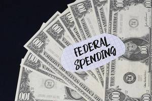 "Federal spending" Text auf kariertem Zettel mit 100-Dollar-Scheinen