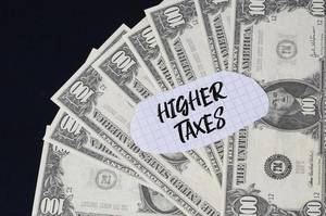 "Higher taxes" Text auf kariertem Zettel mit 100-Dollar-Scheinen