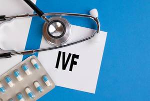 "IVF" / Künstliche Befruchtung, geschrieben auf blauem Ärzteordner, neben Medikamenten und Stethoskop