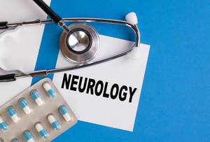 "Neurology" / Neurologie, geschrieben auf blauem Ärzteordner, neben Medikamenten und Stethoskop