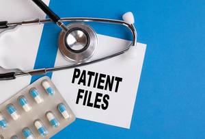 "Patient Files" / Patientenakten, geschrieben auf blauem Ärzteordner, neben Medikamenten und Stethoskop