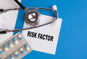 "Risk factor" / Risikofaktor, geschrieben auf blauem Ärzteordner, neben Medikamenten und Stethoskop