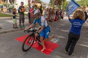 A barefoot woman jumps on her bike at a triathlon in Paguera