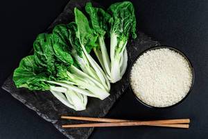 A bowl of rice, chopsticks and cabbage Pak Choi baby on a black background, top view (Flip 2020)
