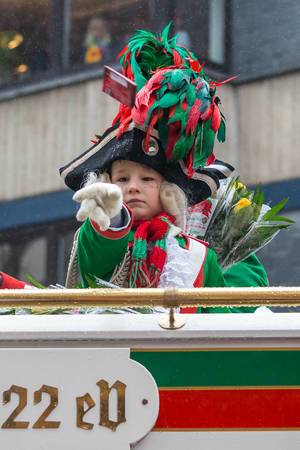 A child wearing the traditional green-red costume and the sophisticated headgear with feathers of the Altstädter Köln 1922 eV. throws sweets from the float to the public during the Rose Monday parade in Cologne