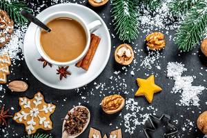A cup of coffee with gingerbread and winter spices on the background with snow and Christmas tree branches. Winter mood