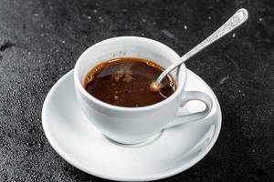 A Cup of hot coffee with a coffee spoon on a dark background