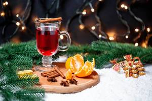 A glas of mulled wine with tangerines, cinnamon and christmastree branches on round cutting board
