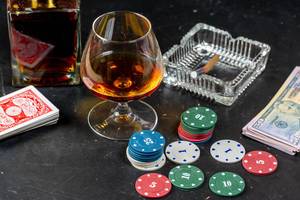A glass of cognac with poker cards, money and chips