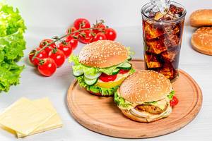 A glass of Cola with ice and fresh burgers on a round kitchen Board