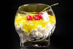 A glass of cottage cheese dessert with fresh kiwano and red currants on a black background