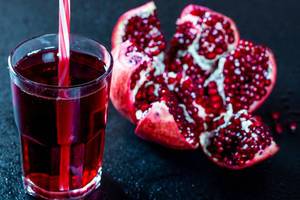A glass of pomegranate juice with fresh pomegranate on a dark background