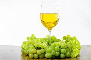 A glass of white wine surrounded by bunches of green grapes (Flip 2019)