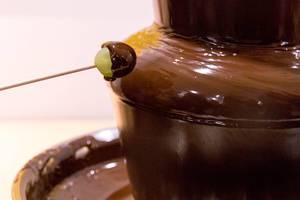 A grape covered in the chocolate of a chocolate-fountain