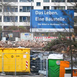 A large construction site in front of a building with a sign in German "Life is a construction site" taken from the Bible