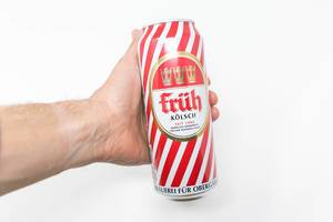 A man holds a red-white can of Früh Kölsch in his hand on a white background. Früh has over 110 years