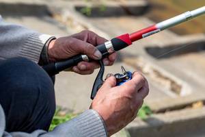 A man prepares a spinning reel for fishing. The concept of a hobby