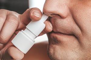 A man sprays medicine in his nose. Runny nose treatment concept