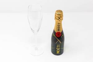 A mini bottle of Moët & Chandon Impérial with an empty champagne glass on white background: the miniature version of a real champagne icon