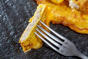 A piece of chops in egg batter on a fork