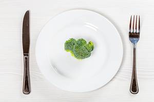 A piece of fresh broccoli on a white plate with a knife and fork. The concept of healthy plant foods (Flip 2019)