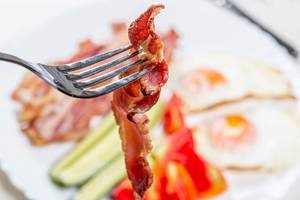 A piece of fried smoked bacon on a fork closeup