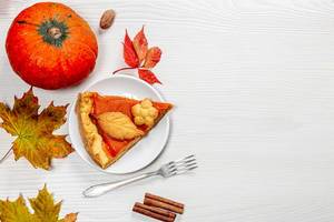 A piece of homemade pumpkin pie with fresh ripe pumpkin, autumn leaves and a fork on the table. The view from the top (Flip 2019)