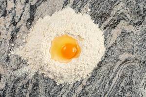 A pile of Flour on a gray Marble slab with egg on the top