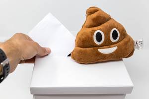 A pile of poo emoji-pillow on a ballot box, while a man is voting