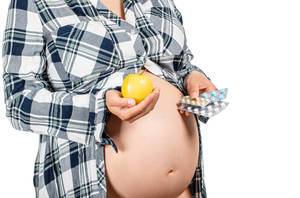 A pregnant woman holds an apple in one hand and medicines in the other