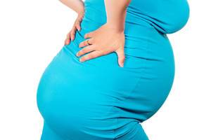 A pregnant woman holds her hands behind her back. Concept of pain, difficulties and problems of pregnant women