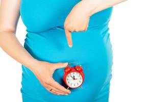 A pregnant woman points to her stomach and watch. The concept of waiting, time